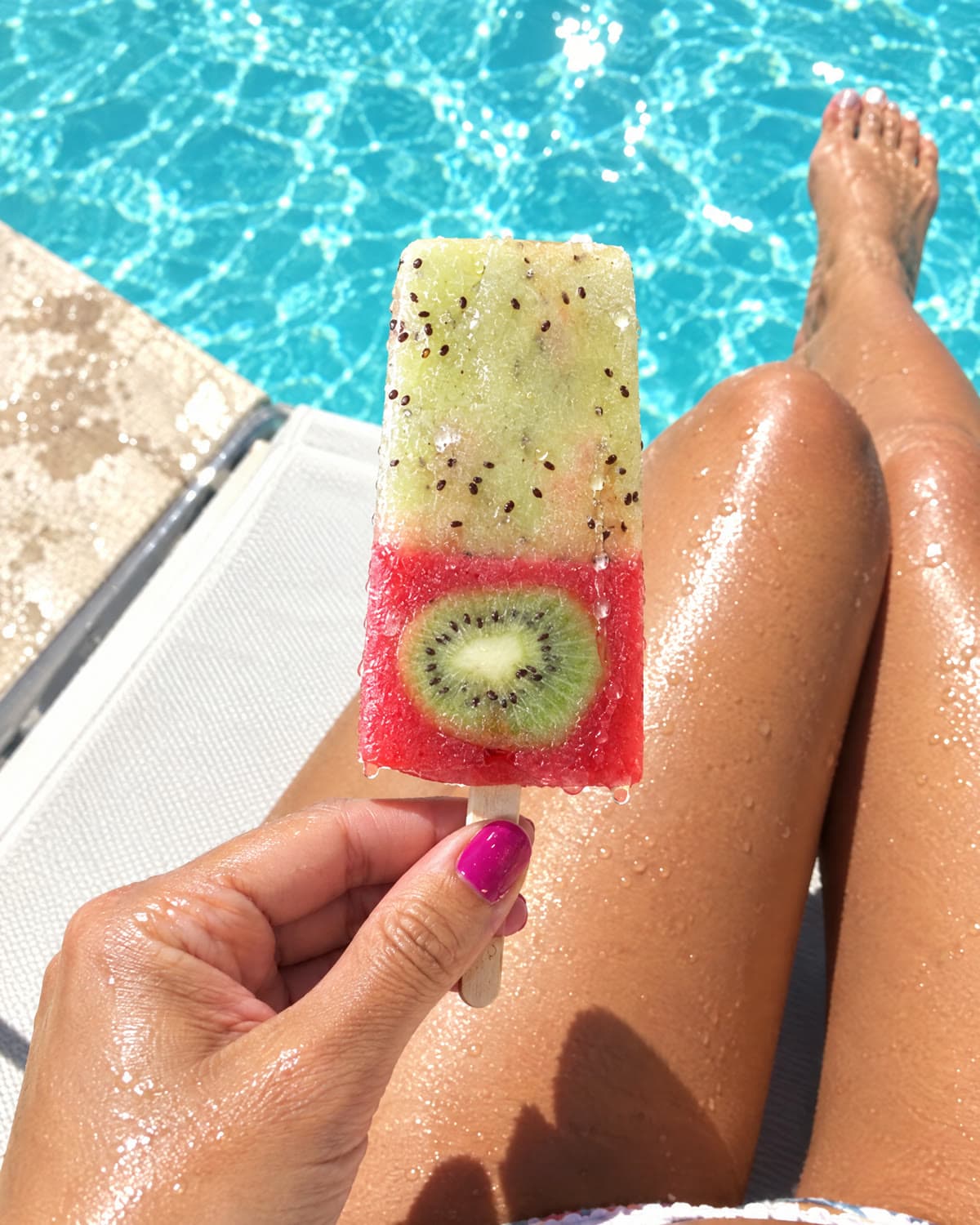 A kiwi strawberry pop held over a turquoise pool.